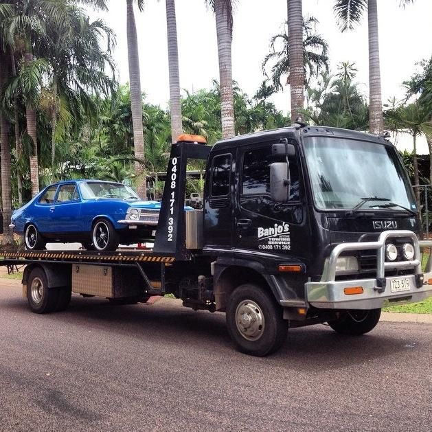 Black Tow Truck With a Blue Car on Its Flatbed, on a Road With Palm Trees — Banjo's Anytime Towing in Winnellie, NT