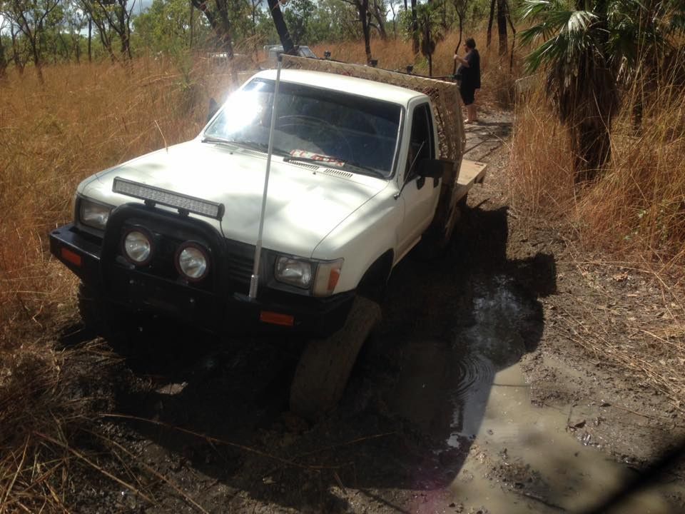 White Pickup Truck Stuck in Mud on a Dirt Road, Surrounded by Tall Dry Grass — Banjo's Anytime Towing in Berrimah, NT