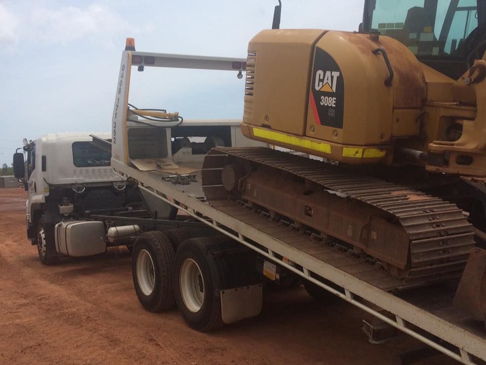 Flatbed Truck Carrying a Caterpillar Excavator on a Dirt Road — Banjo's Anytime Towing in Coolalinga, NT