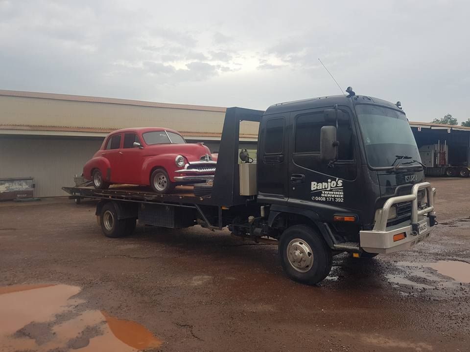 Red classic car on a black tow truck in a muddy lot — Banjo's Anytime Towing in Humpty Doo, NT