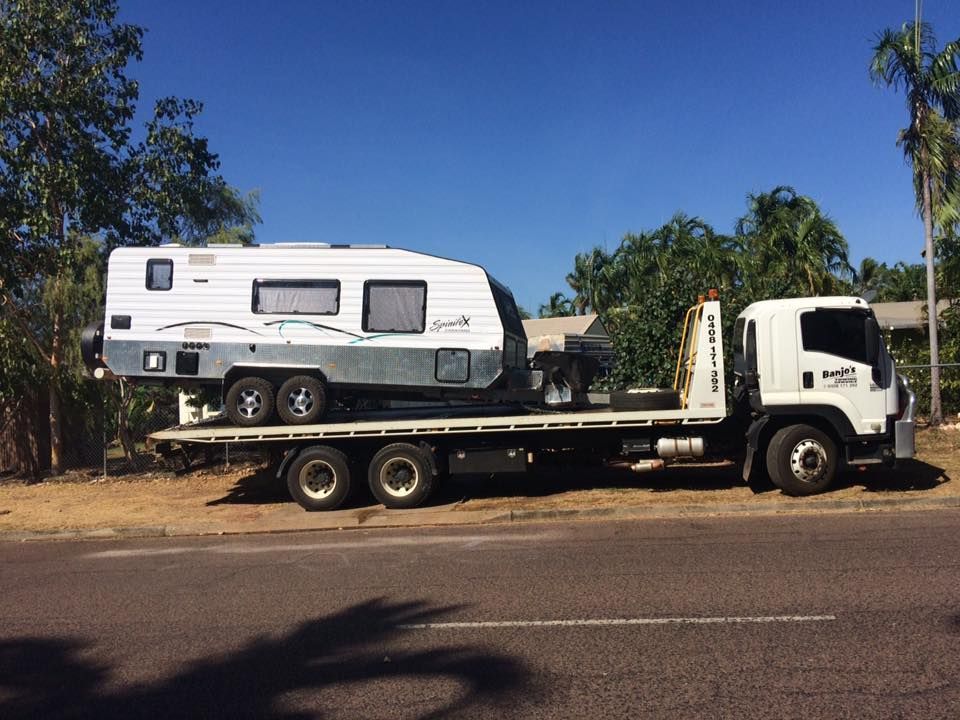 A white caravan loaded on a flatbed tow truck on a road under a blue sky — Banjo's Anytime Towing in Humpty Doo, NT