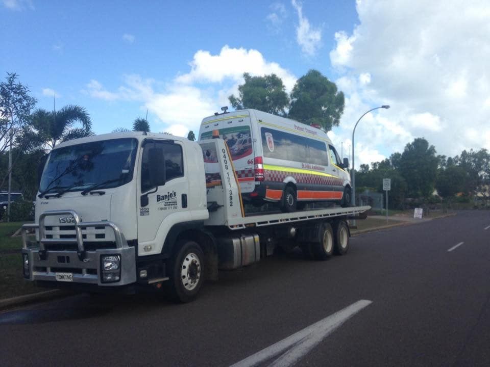 White SUV on a tow truck, driving on a road, under a cloudy sky — Banjo's Anytime Towing in Humpty Doo, NT