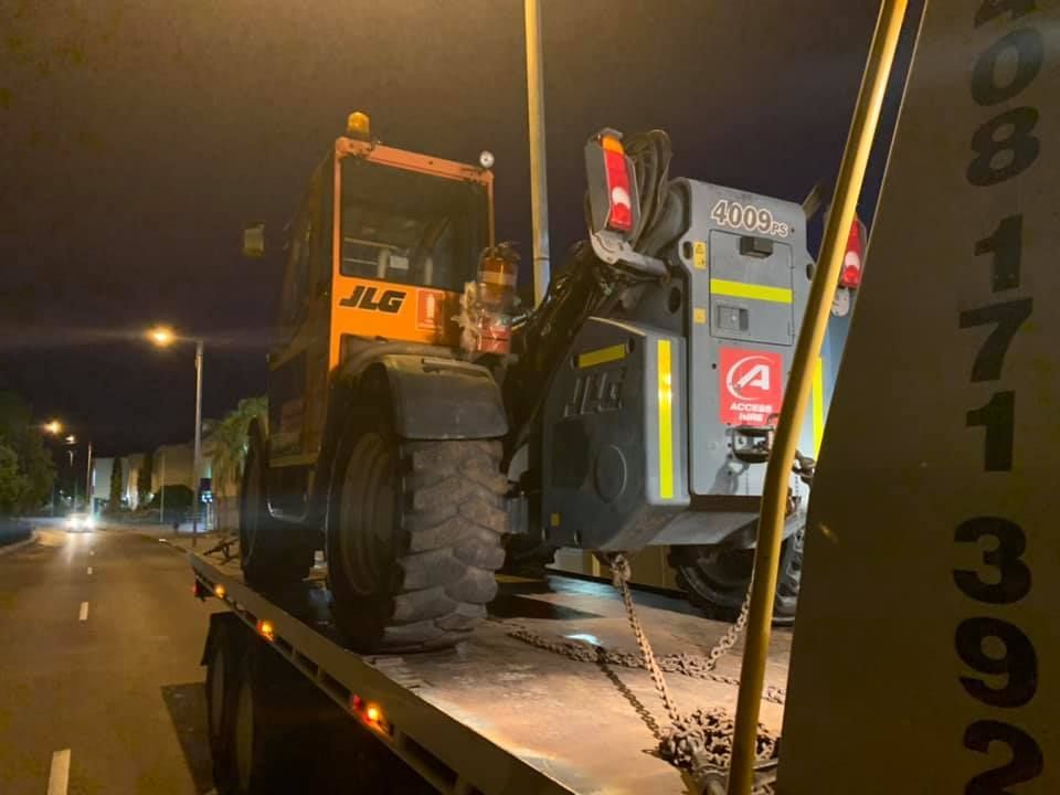 JLG Telehandler on a flatbed truck at night on a street, with streetlights — Banjo's Anytime Towing in Humpty Doo, NT