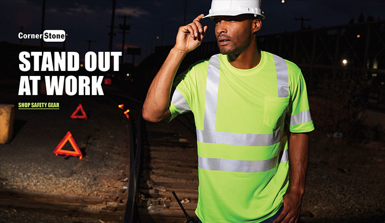 Man wearing neon work shirt and hard hat, standing near railroad tracks, 