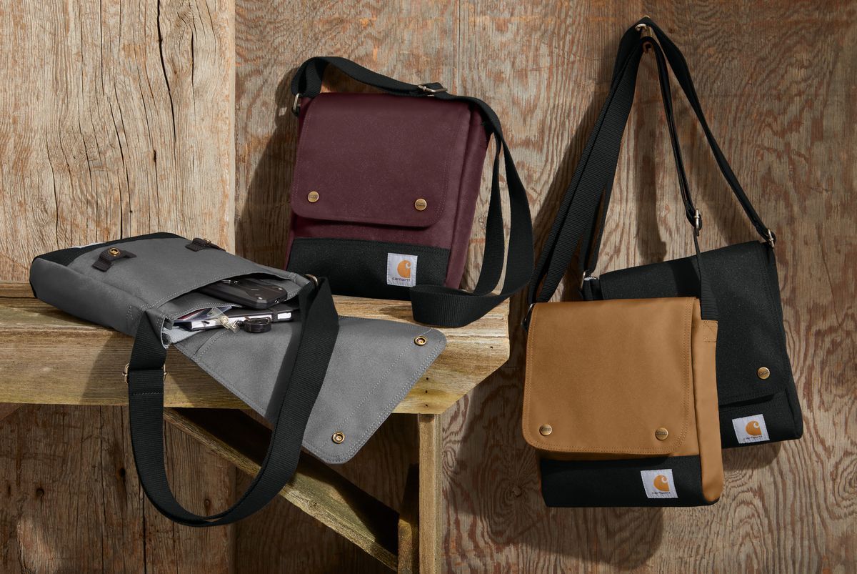 Four Carhartt messenger bags in various colors on wooden surface.