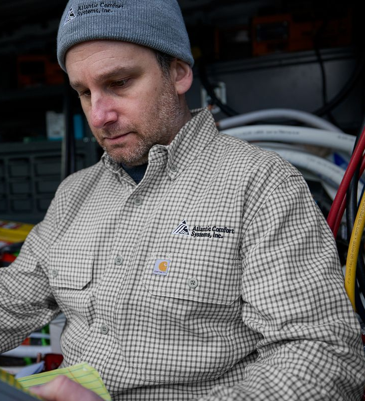 Man in a gray beanie and plaid shirt reviews paperwork inside a van filled with tools and hoses.