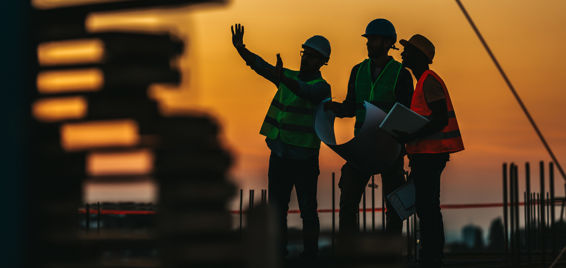Construction workers looking at plans on a building site at sunset.