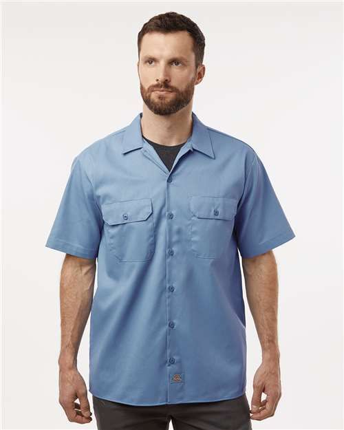 Man wearing a light blue short-sleeved button-up shirt with two pockets.