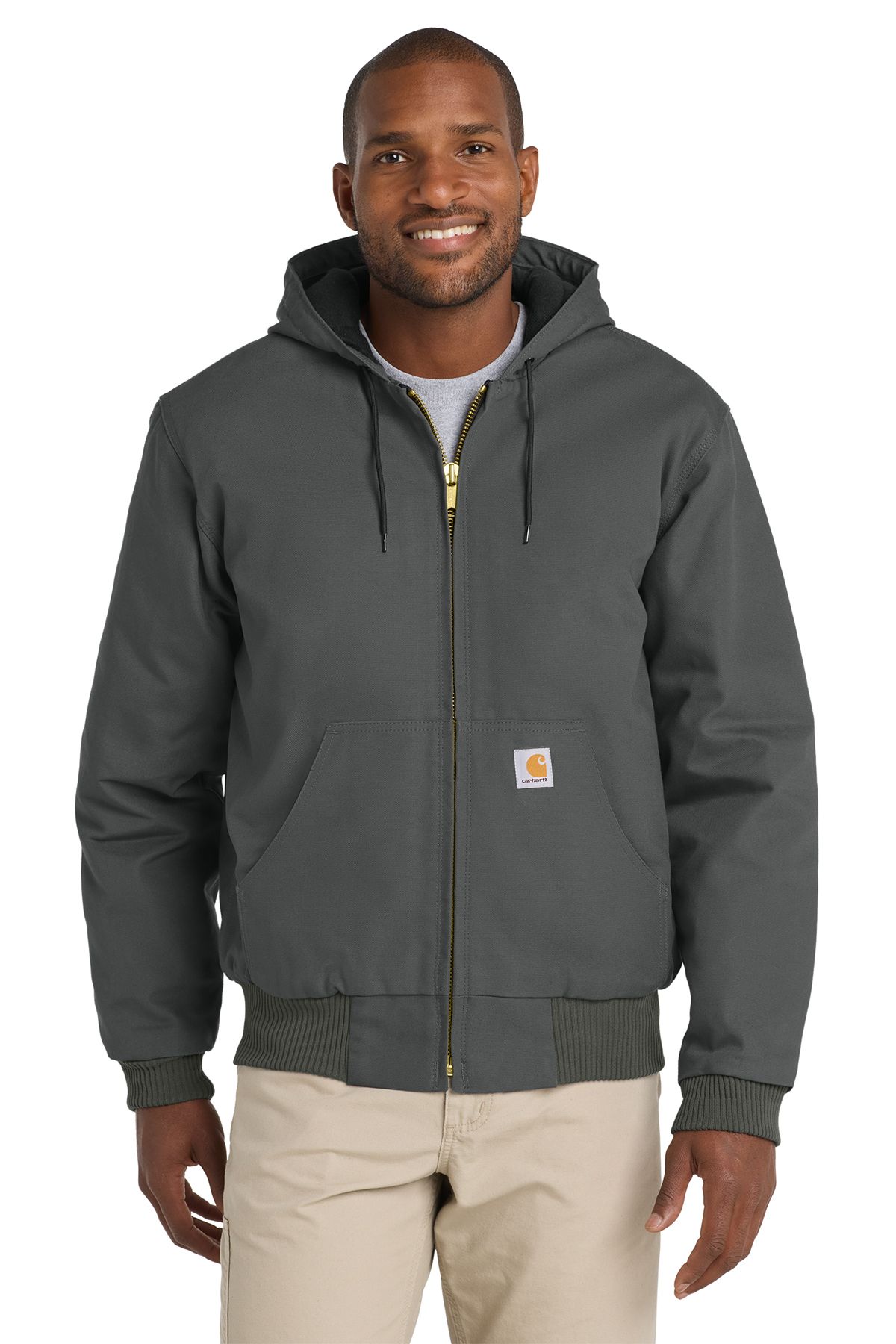 Man in gray hooded Carhartt jacket, khaki pants, smiling, outdoors.