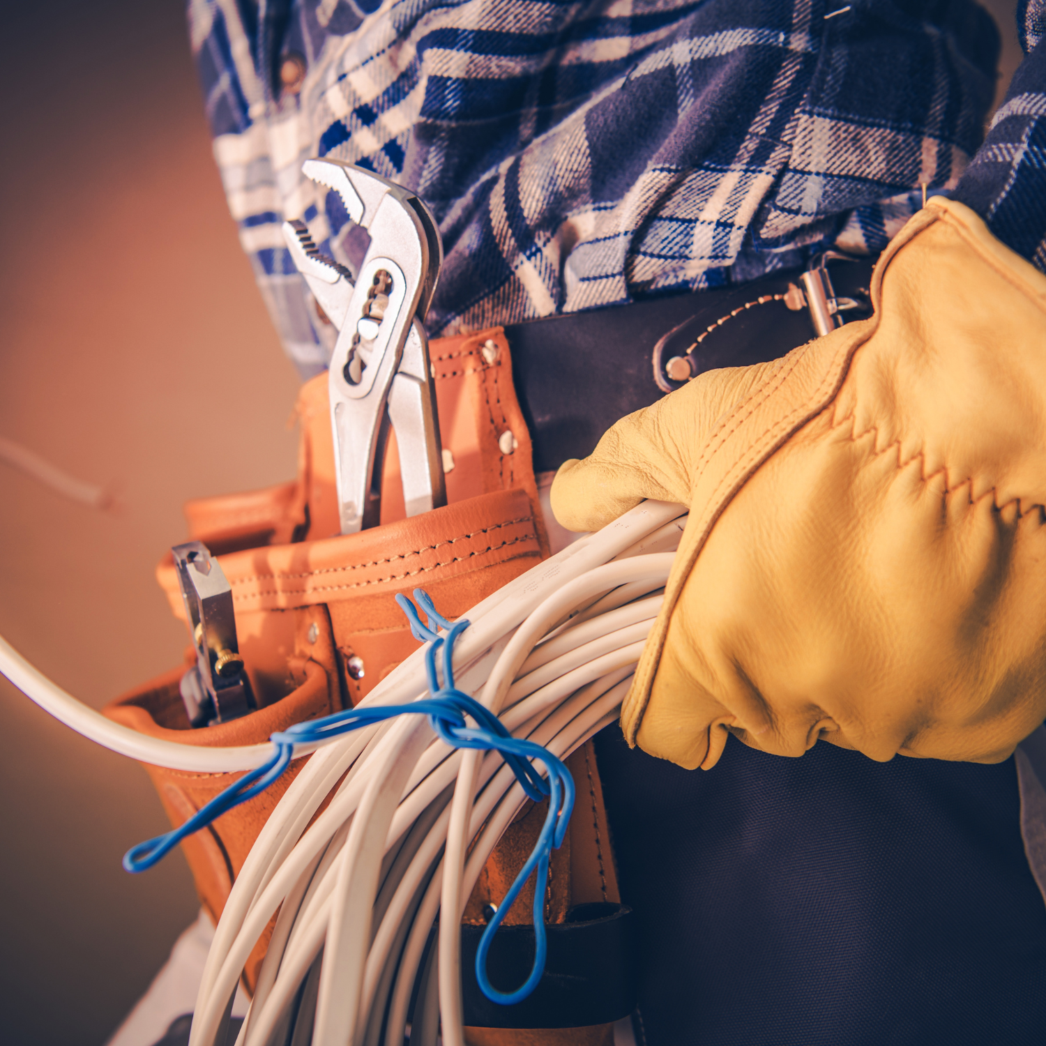 Electrician with tool belt and gloves holding electrical wire.