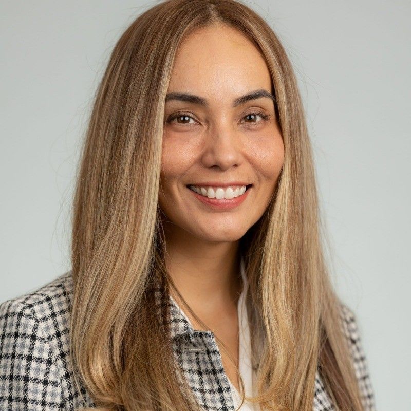 A woman with long blonde hair is smiling and wearing a plaid jacket.