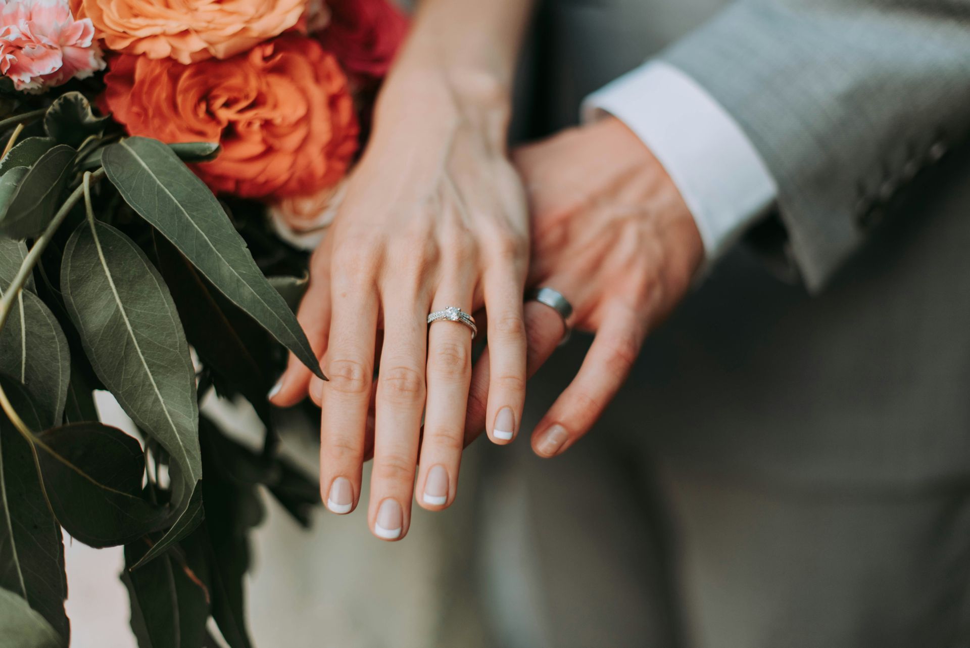 A bride and groom are holding hands with their wedding rings on their fingers.