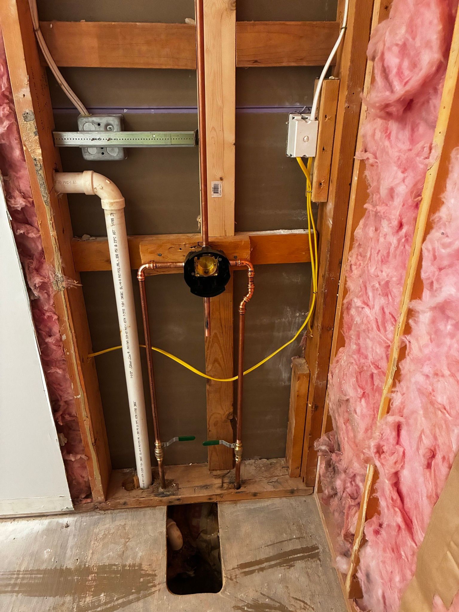 Interior wall framing showing installed plumbing and electrical wiring with pink insulation in the side studs.