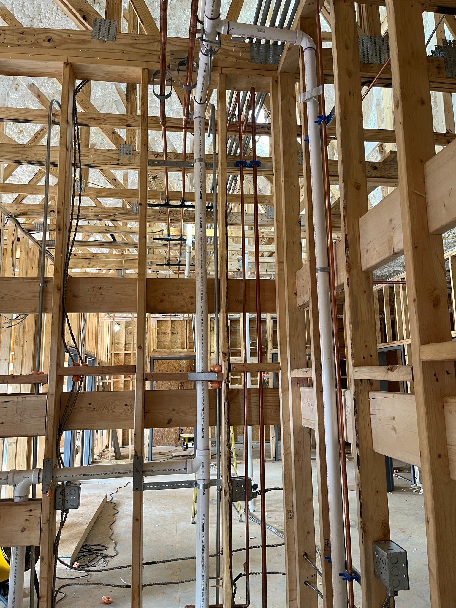 The interior framing of a house under construction, showing exposed wooden studs and installed plumbing and electrical lines.