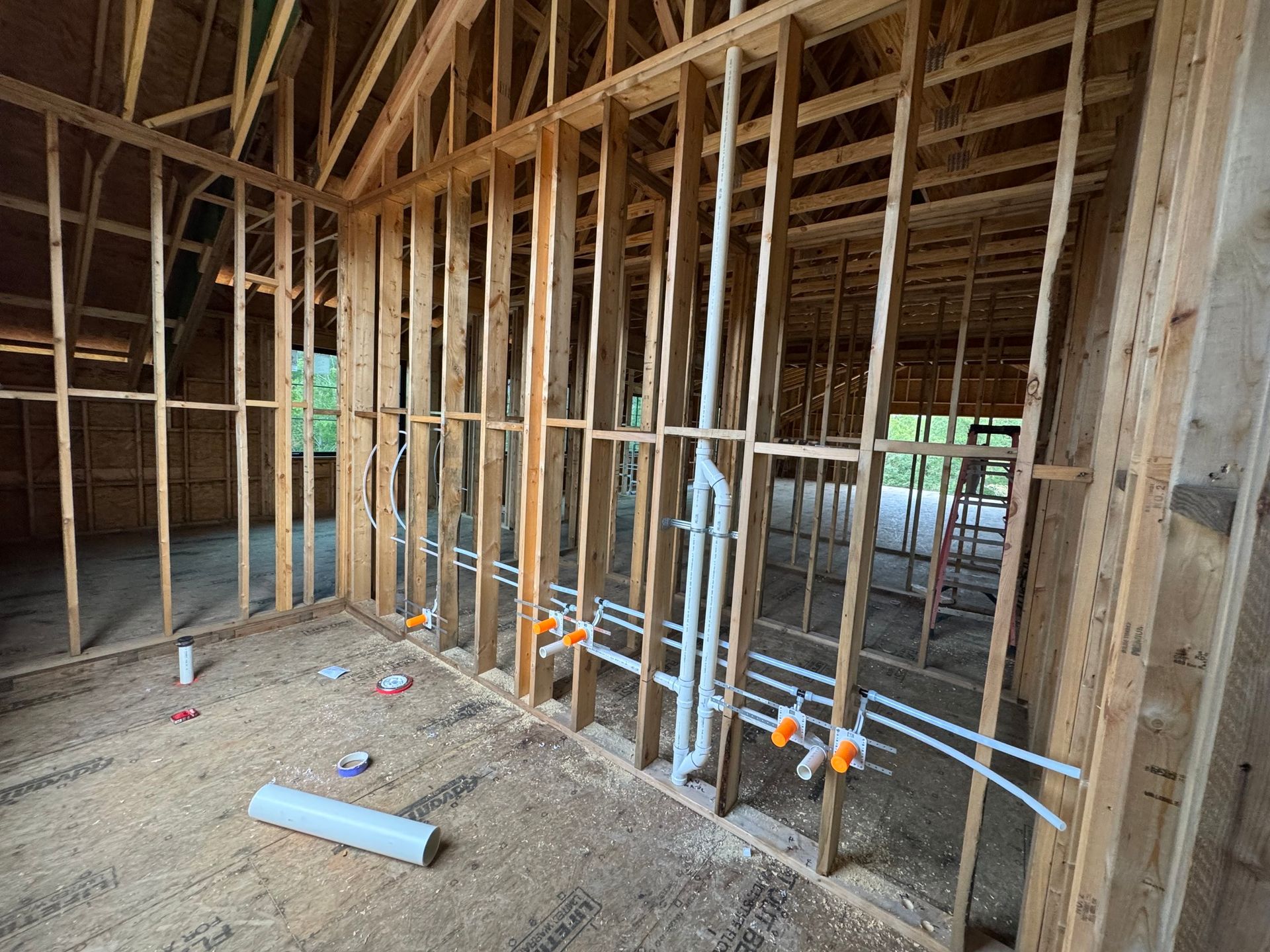 Wooden framing of a room under construction with exposed PVC plumbing and PEX water lines running through the studs.