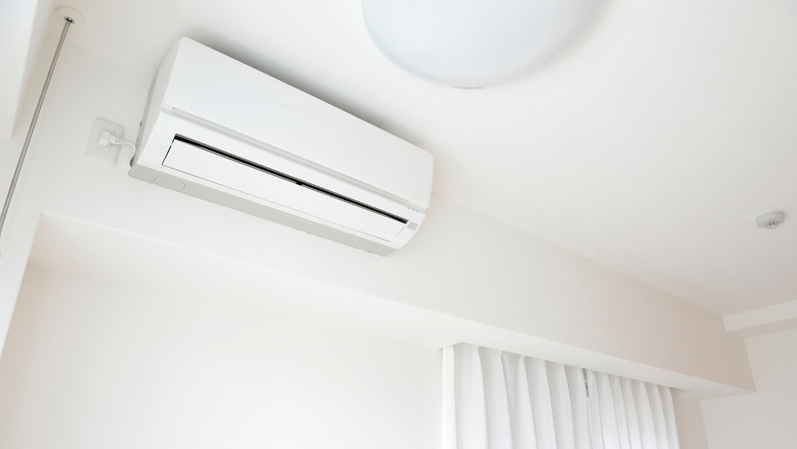 White wall-mounted air conditioner near a ceiling light in a bright room