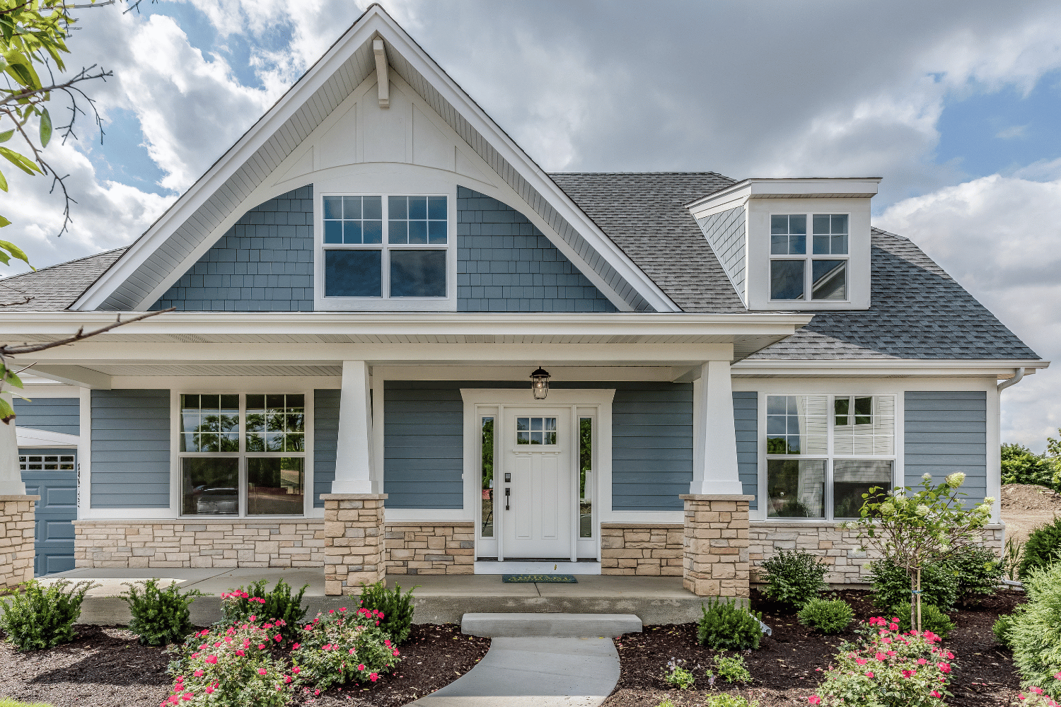 Blue-gray suburban house with white trim, stone porch columns, and a manicured front garden
