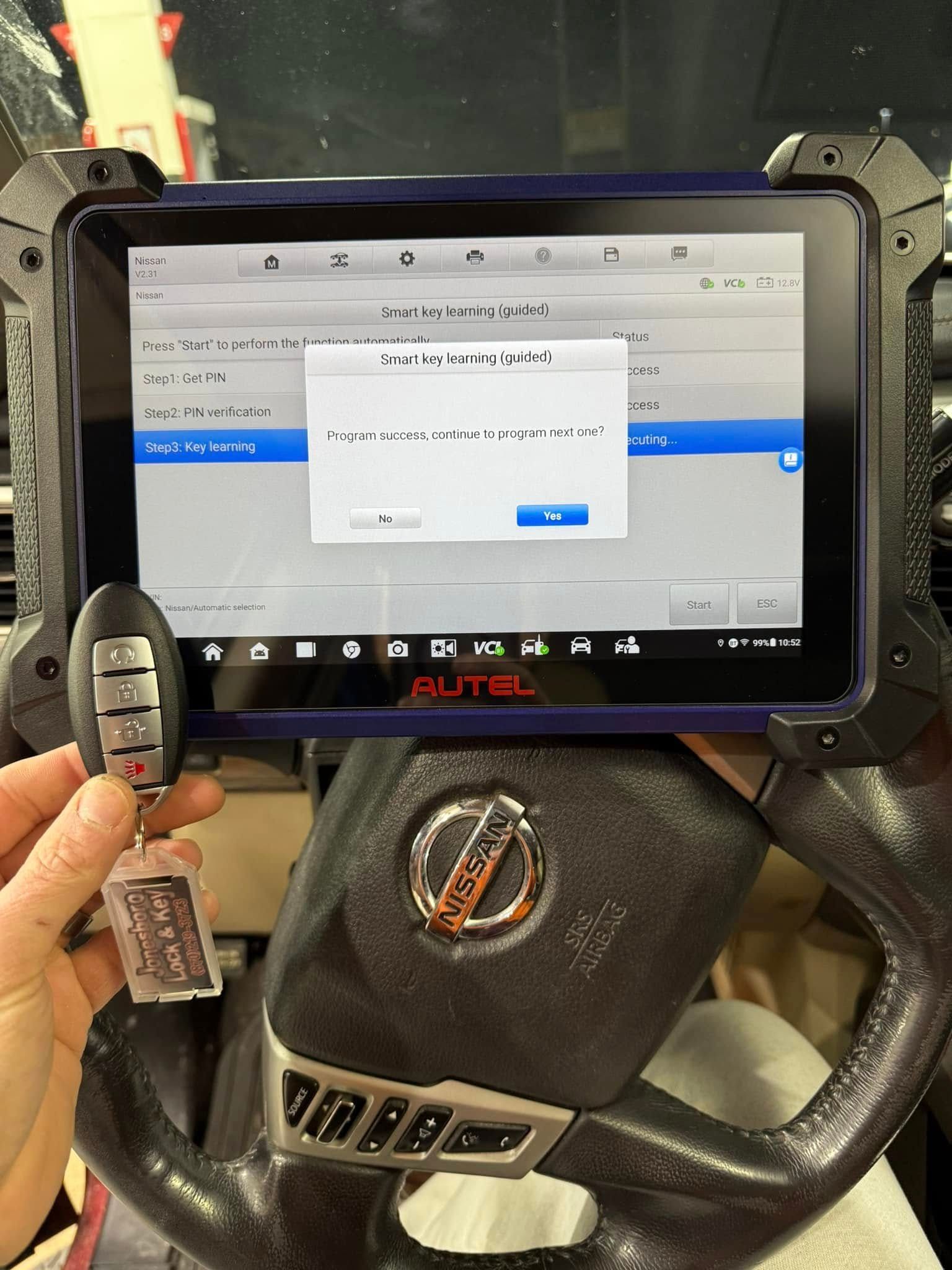 A person is holding a car key in front of a tablet.