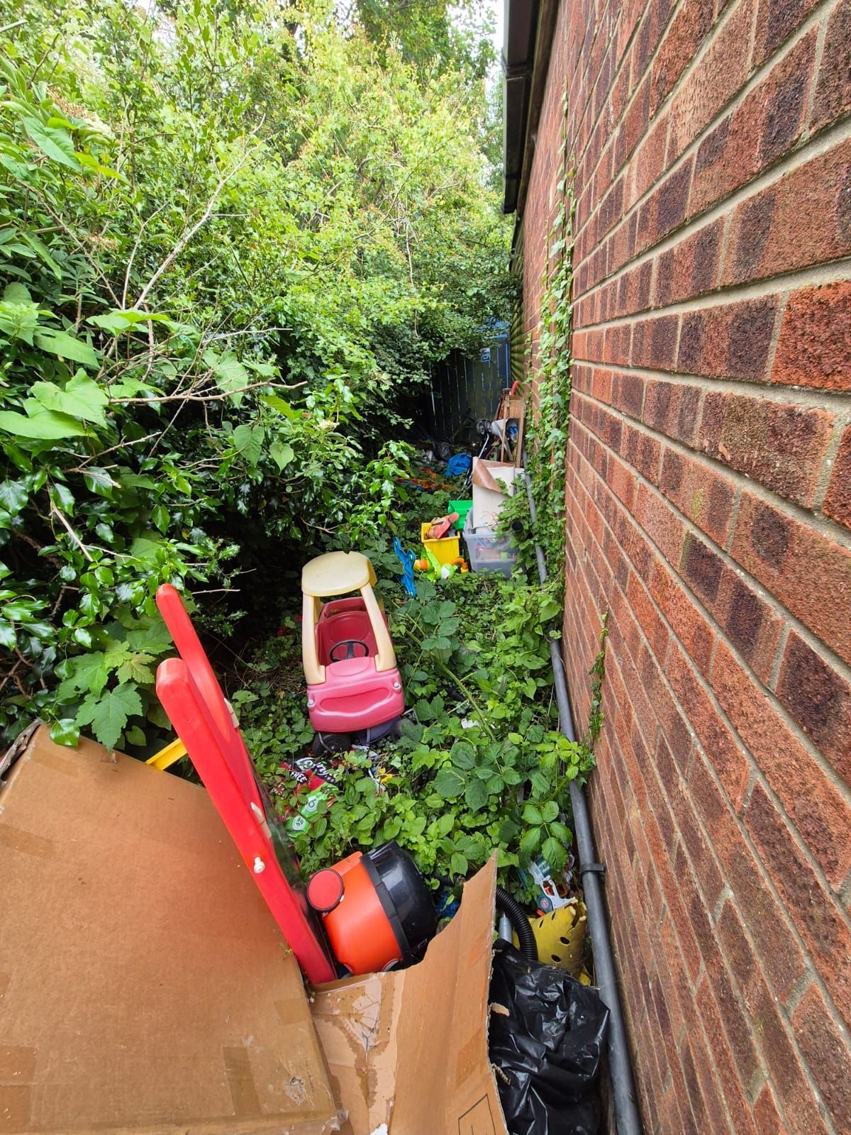 A cardboard box filled with toys is sitting next to a brick wall.