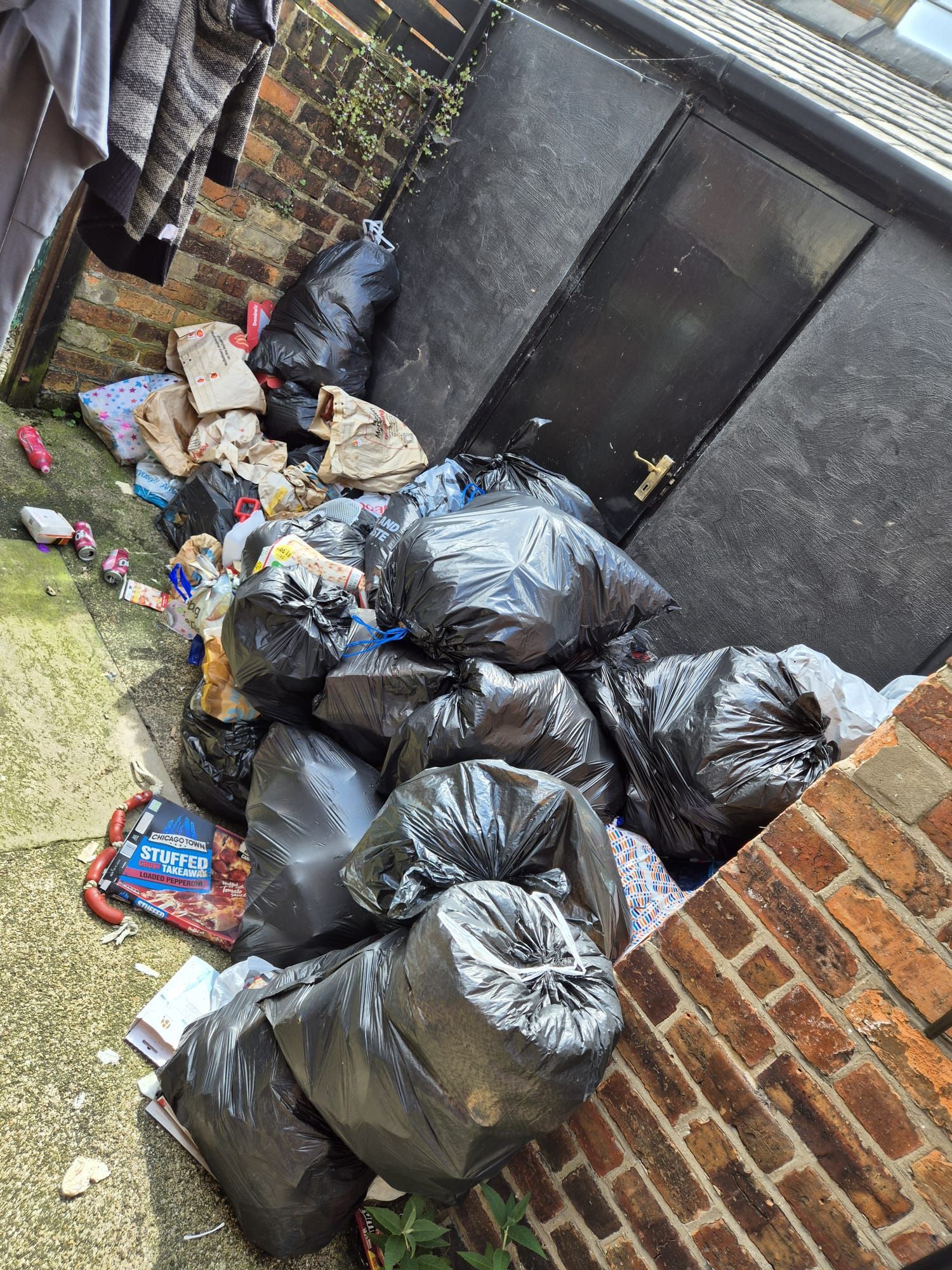 A pile of garbage bags is sitting in front of a brick building.