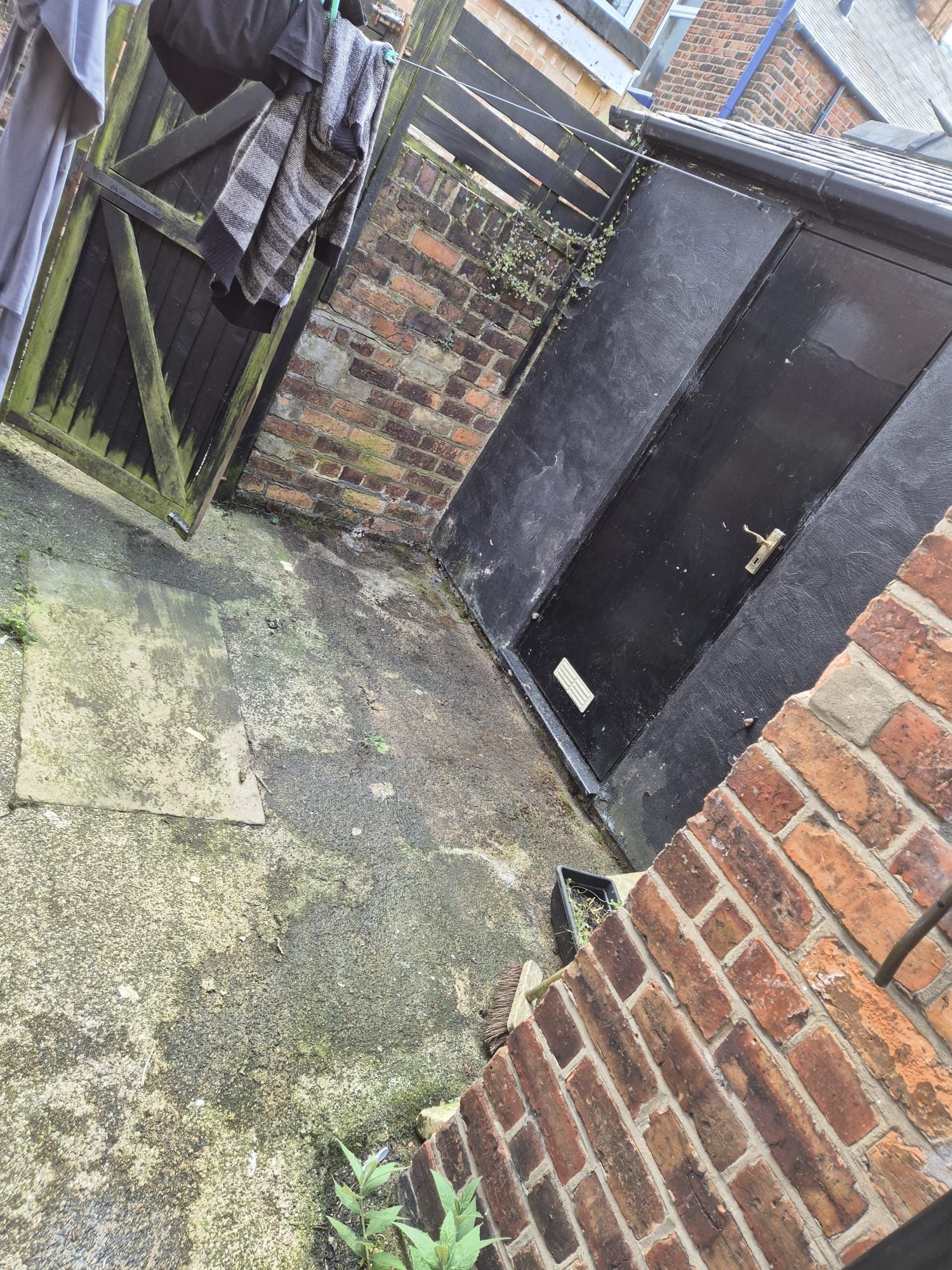 A brick wall with a black door and clothes hanging on it.