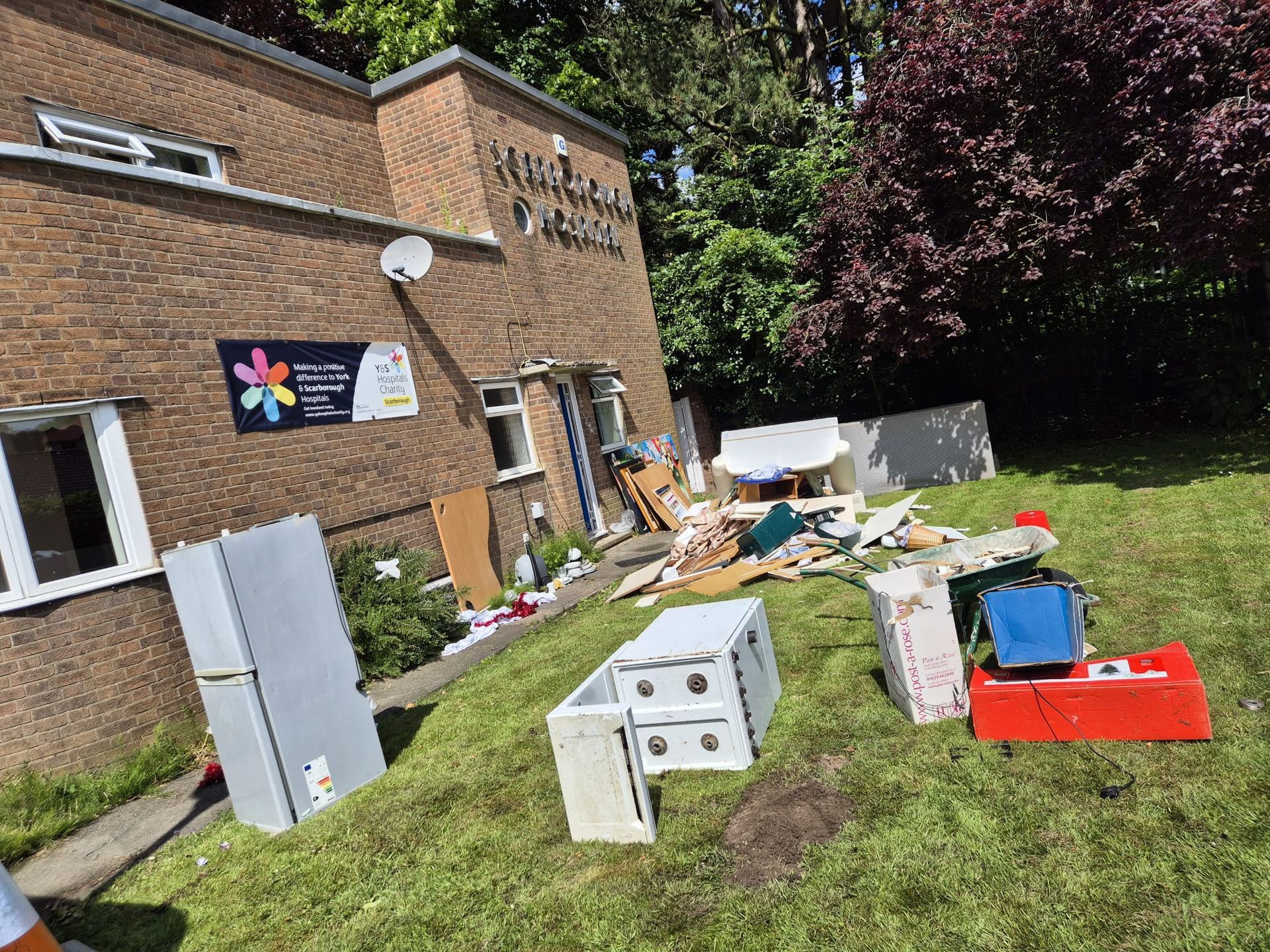 A pile of junk is sitting on the grass in front of a brick building.