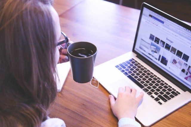 woman holding a mug of coffee looking for a therapist on line on laptop