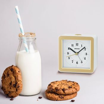 A clock next to a bottle of milk and chocolate chip cookies