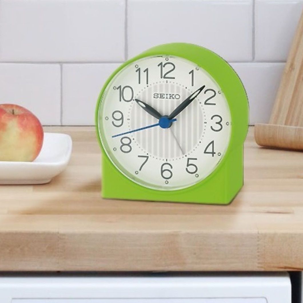 A green seiko clock sits on a wooden counter