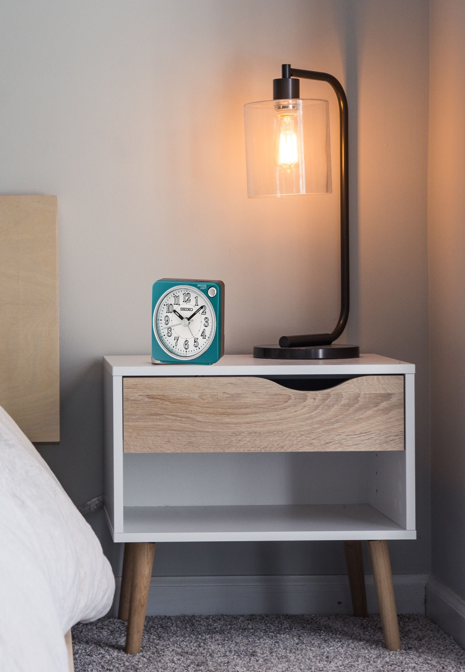 A nightstand with a lamp and a clock on it in a bedroom.