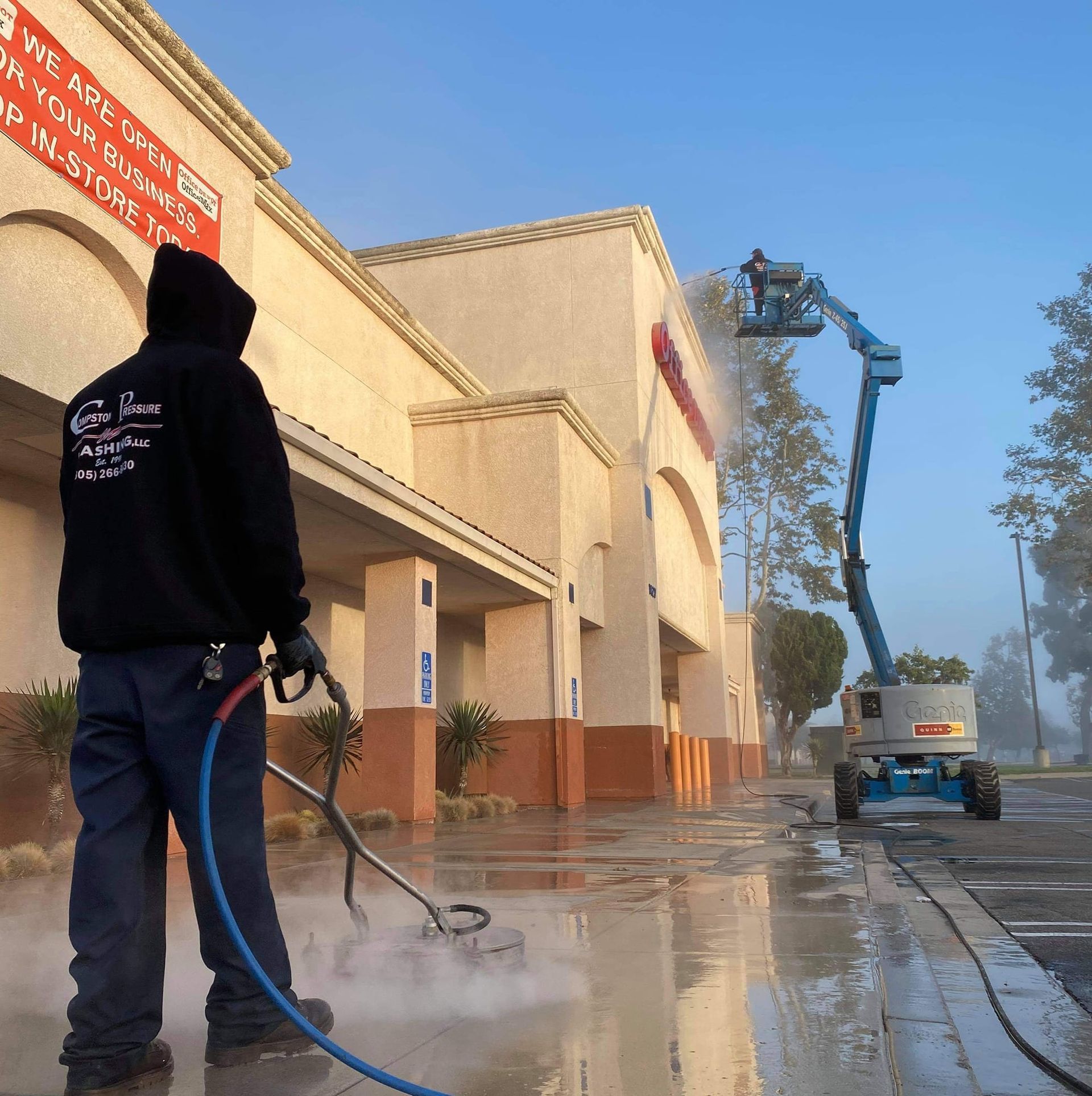 A man in a black hoodie is cleaning a building with a hose