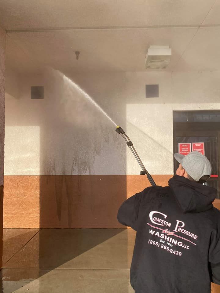 A man is cleaning a building with a high pressure washer.