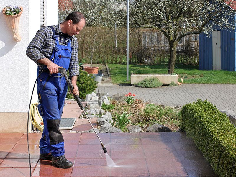 A man is using a high pressure washer to clean a patio
