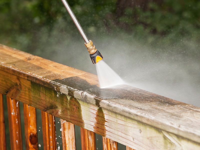 A person is using a high pressure washer to clean a wooden deck.