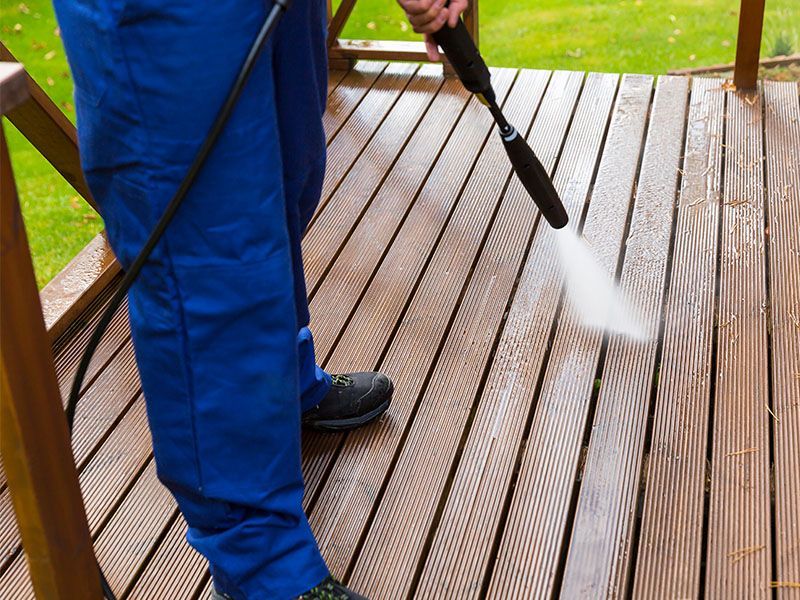 A person is using a high pressure washer to clean a wooden deck.