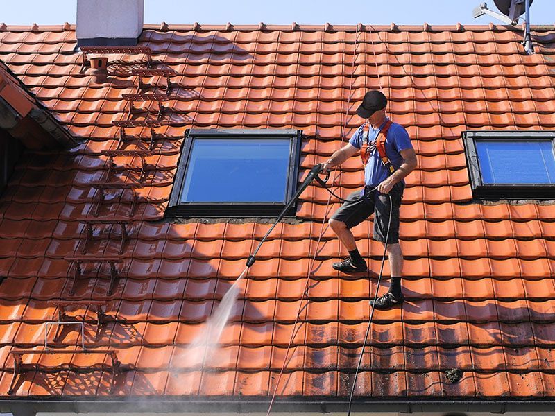 A man is cleaning the roof of a house with a high pressure washer.