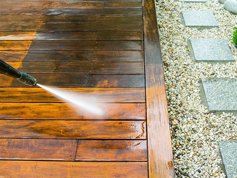 A person is cleaning a wooden deck with a high pressure washer.