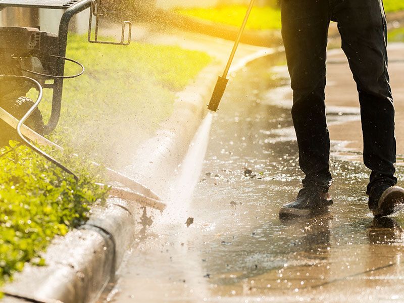 A man is using a high pressure washer to clean a sidewalk.