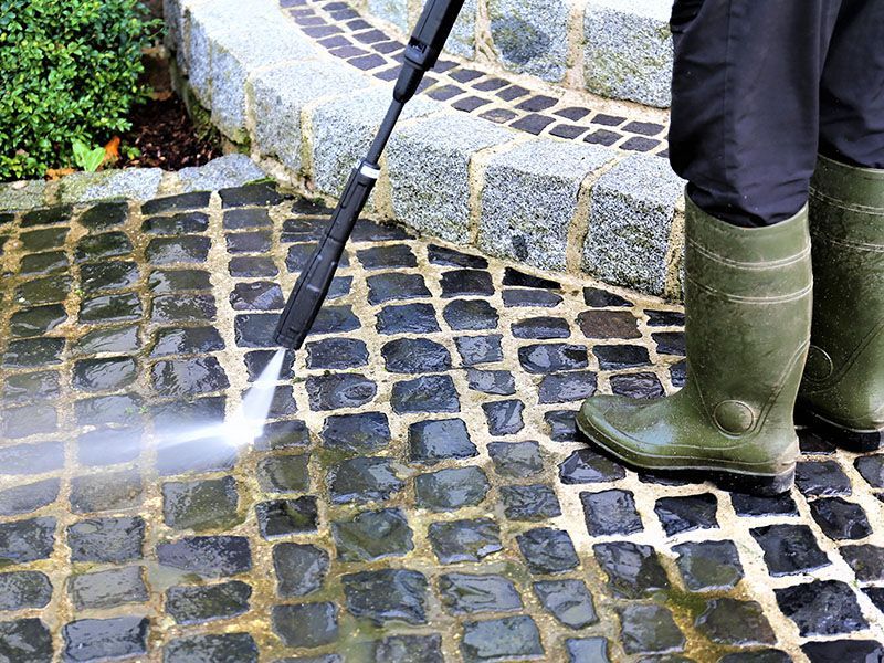 A person is using a high pressure washer to clean a cobblestone driveway.