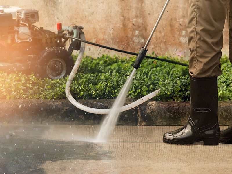 A person is using a high pressure washer to clean a sidewalk.