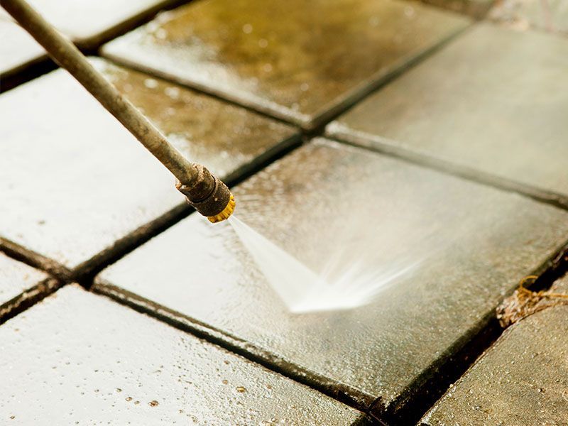 A person is using a high pressure washer to clean a tiled floor.