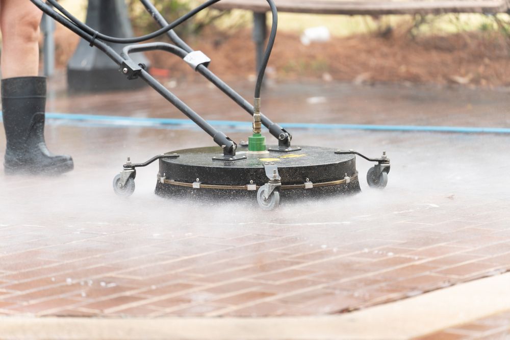 A person is using a high pressure washer to clean a brick walkway.