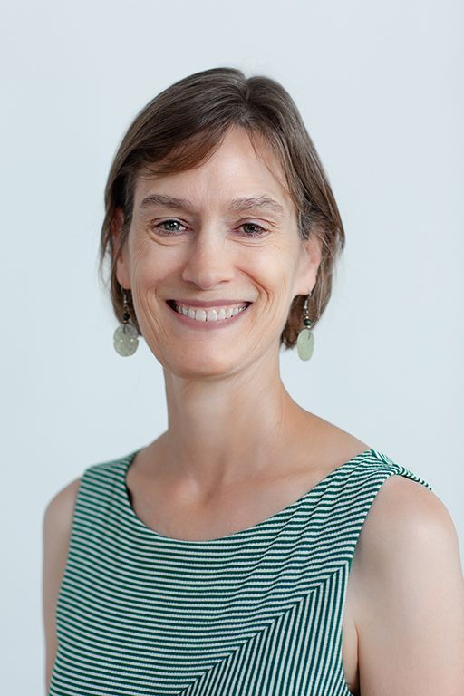 Woman with short brown hair smiles, wearing a green striped top and earrings. Against a white background.