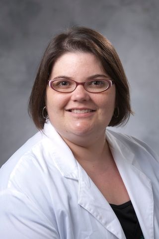 Woman in glasses and white lab coat smiles at the camera.