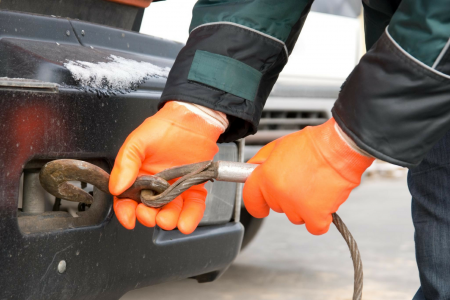 Person in orange gloves attaching a tow cable to the hitch of a car.