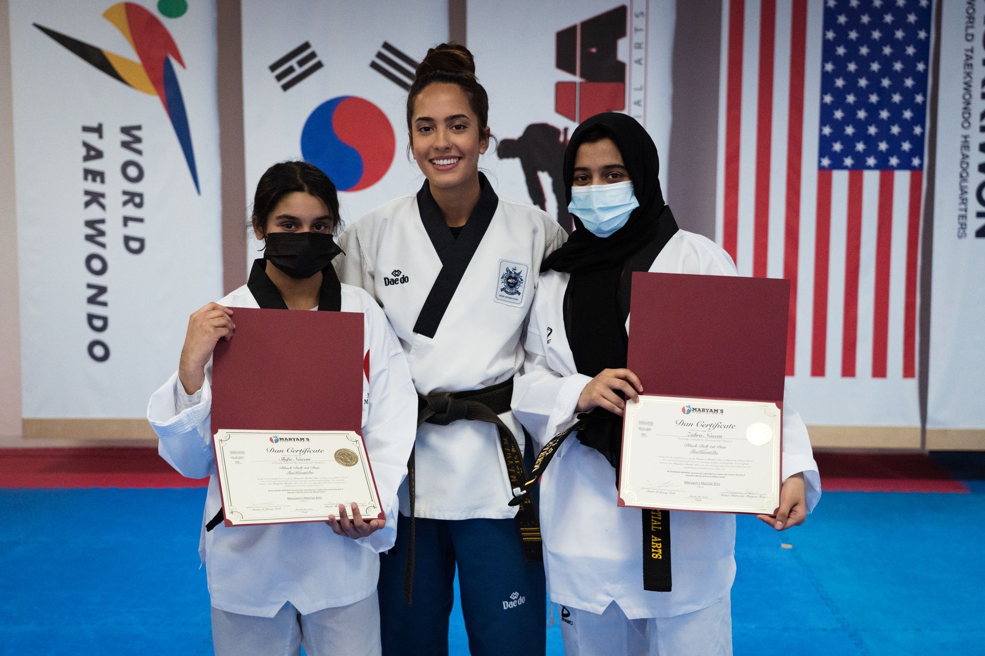 Three women in taekwondo uniforms are posing for a picture while holding certificates.