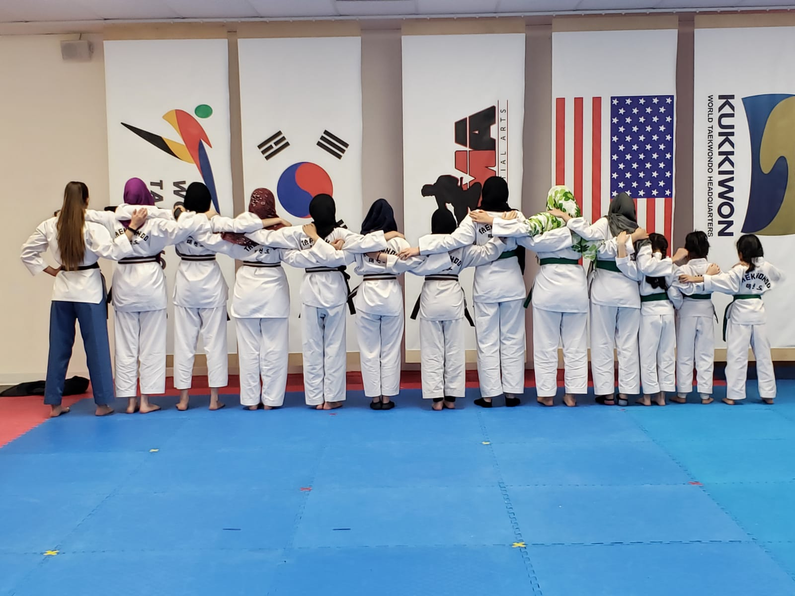 A group of people in karate uniforms are standing on a blue mat.