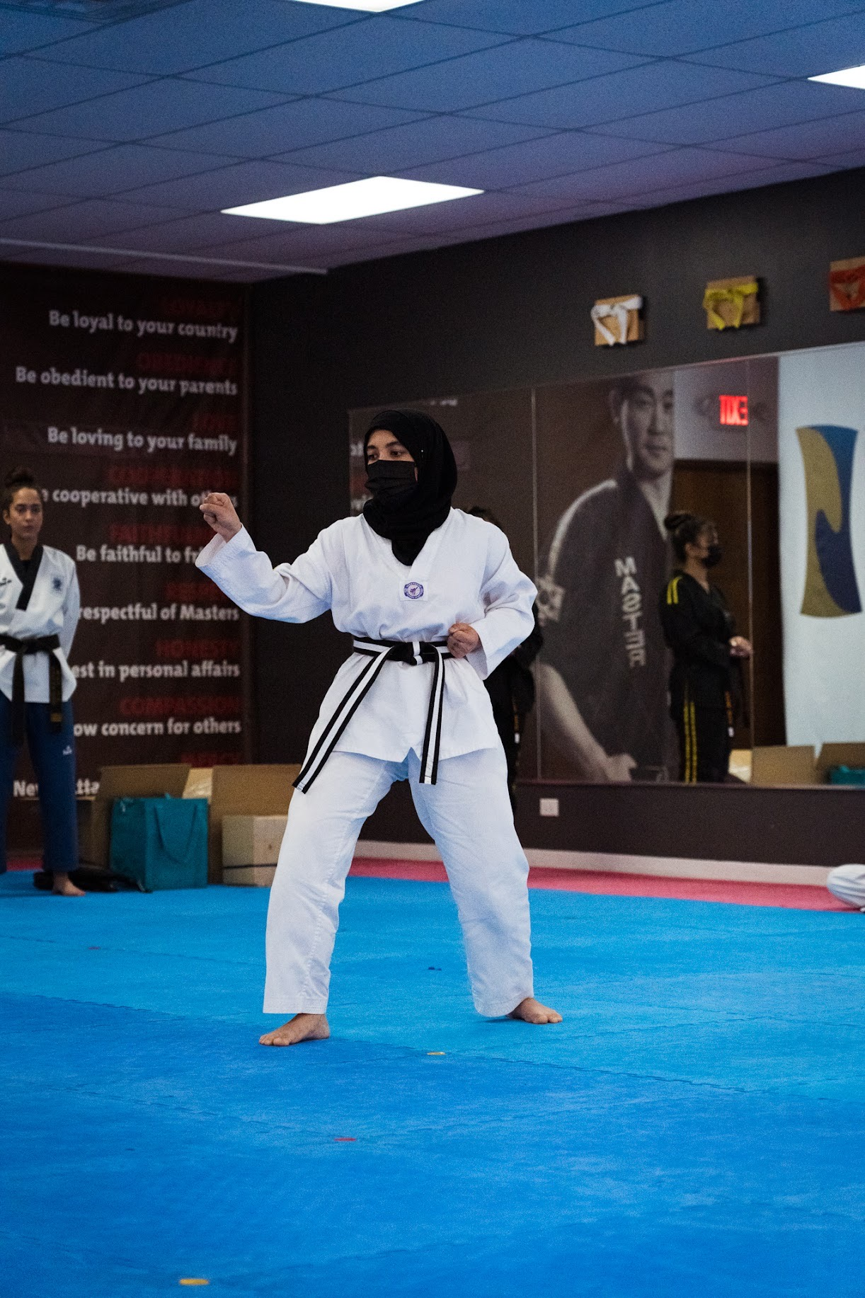 A woman in a hijab is practicing martial arts on a blue mat
