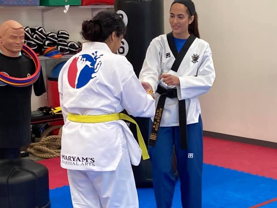 Two women in martial arts uniforms are standing next to each other in a gym.