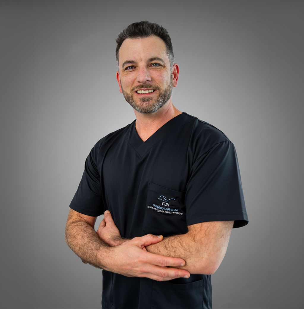 Um homem de camisa preta com os braços cruzados está sorrindo para a câmera.